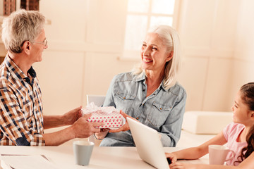 Obraz premium This is for you. Thoughtful mature gentleman smiling to his beautiful wife while giving her a beautifully wrapped present.