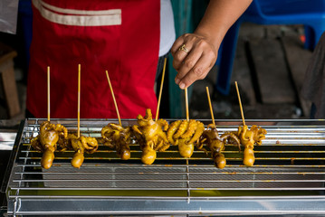 Grilled squid cover yellow sauce in skewers on grid iron, Thai local style Delicious barbeque sea food at Thailand seafood in night street food market.