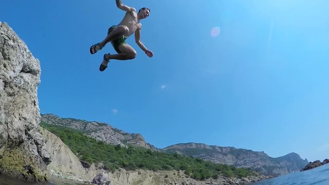 A man with a running start dives into the sea from the cliff. Slow motion.