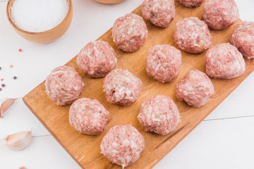 Raw meatballs on a wooden cutting board with ingredients - top view