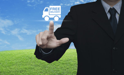 Businessman pressing free delivery truck icon over green grass field with blue sky, Business transportation concept