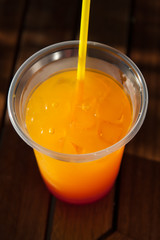 Multicolored cocktail with ice in a plastic cup with a straw