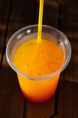 Multicolored cocktail with ice in a plastic cup with a straw