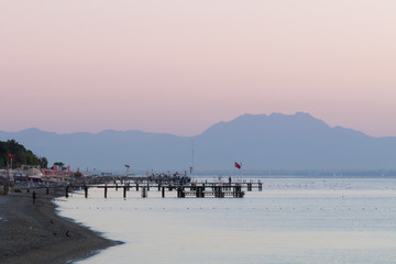 Dawn on the sea beach. Pier. The mountains in the morning mist are far away.