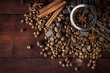 Dark chocolate, spices, coffee beans and metal strainer on a wooden background