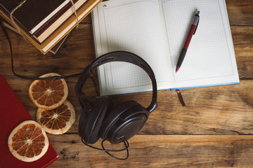 Books, Headphones, open Diary, Pen, Slices of Dried Orange on a wooden background. The concept of Audio Books and Audio Training. Flat lay, top view