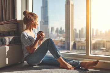 happy young woman drinks coffee in morning at window