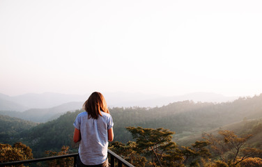 Naklejka premium Happy success woman at sunset or sunrise standing at mountain top looking to beautiful hills