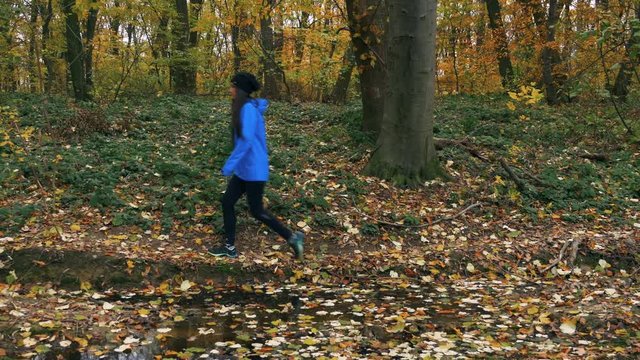 Dolly shot: young woman in blue jacket walking in the autumn woods.