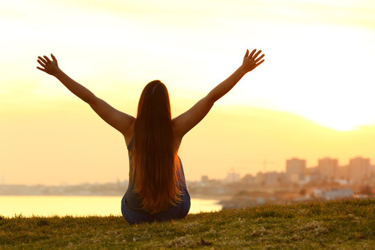 Cheerful woman raising arms at sunset