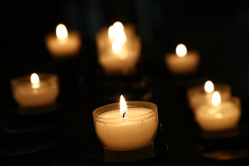 Fototapeta na wymiar White candles burning in dark church close up