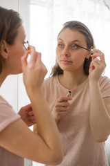 Portrait of attractive young woman putting on makeup at home. Mascara