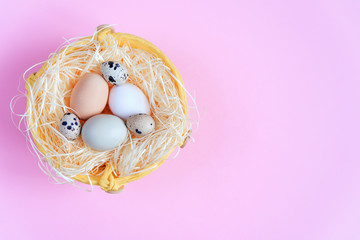 Fototapeta na wymiar Easter eggs of different colors and quail eggs in a wicker basket on a pink background, Top view, Flat lay. Easter concept.