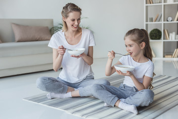 mother and daughter eating cereal meal while sitting on yoga mats