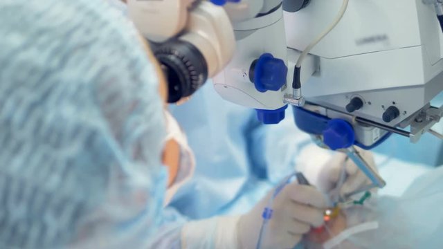 One surgeon is operating an eye while another one is adjusting ocular for observation
