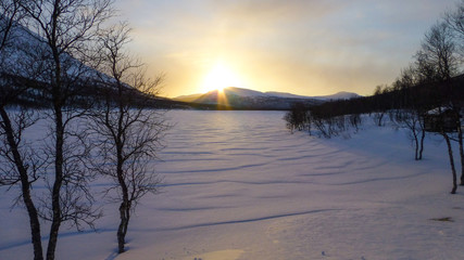 Sunset over a frozen snowy lake up in the mountains of northern Sweden near the polar circle.