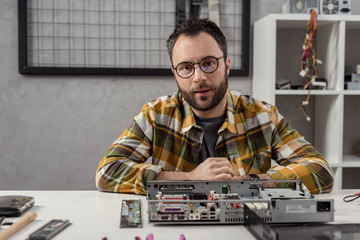 man looking at camera against broken computer on table