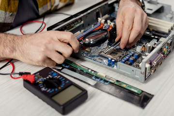 cropped image of hands fixing motherboard of pcwith multimeter