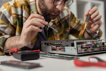 man using multimeter and whisk while fixing computer motherboard