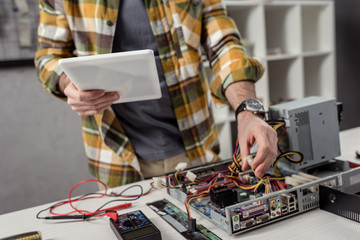 cropped image of man using digital tablet while fixing computer