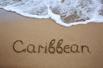 Word Caribbean written on the sand near the sea.