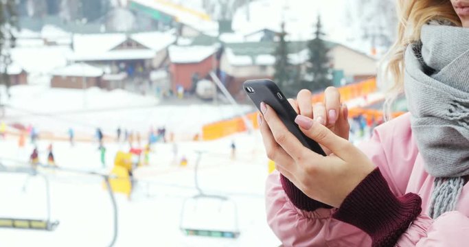 closeup girl hand holding using smart phone outdoor winter mountain resort skiing ski lift tapping touching screen application map gadget tech e-business email typing connect chat online web browser