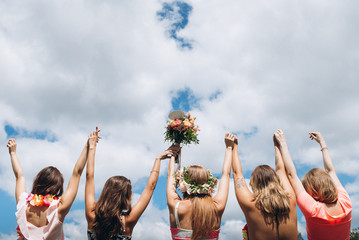 Girls raised their hands up on cloudy sky background at hawaii style hen party