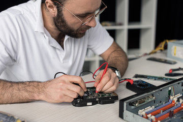 repairman using multimeter while testing hard disk drive