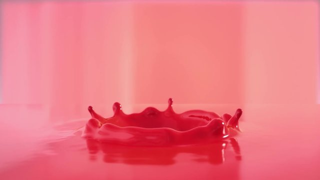 Dropping ball in red paint making beautiful crown splash shooting with high speed camera