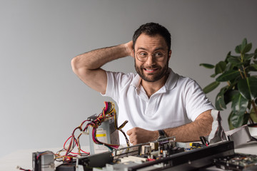 man with facial expression and hand behind head against broken pc