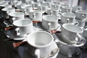 Many rows of white tea cups with saucer and sugar sticks on table