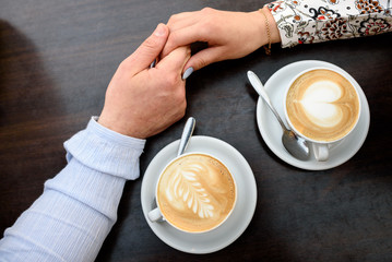 Coffee cups and holding hands at the darken wooden table