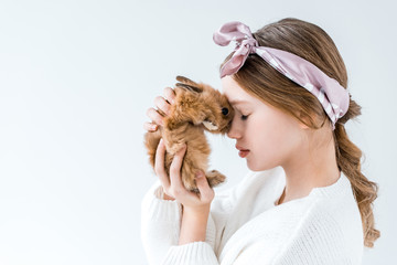 side view of beautiful little girl holding furry rabbit isolated on white