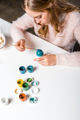 beautiful focused teenage girl painting easter egg at table