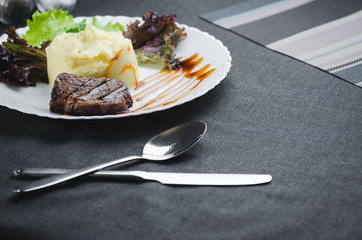 On a white plate, on a beautiful fabric and dark background mashed potatoes with beef meat beautifully polished balsamic sauce