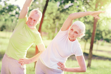 Older and healthier. Waist up of positive friends looking away while doing useful exercises outdoors and having fun © zinkevych