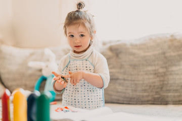 toddler girl in drawing apron draws fingers at home