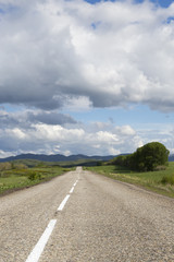 Fototapeta premium A road in the mountains under the sky with clouds and clouds, vertical picture