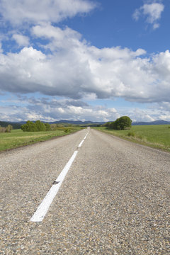 A road in the mountains under the sky with clouds and clouds, vertical picture
