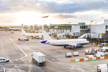 Busy airport view with airplanes and service vehicles at sunset - obrazy, fototapety, plakaty