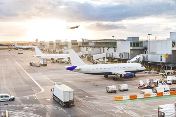 Foto auf Leinwand Blick auf den geschäftigen Flughafen mit Flugzeugen und Servicefahrzeugen bei Sonnenuntergang © william87
