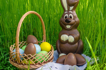 Chocolate Easter bunny with chocolate eggs and sweets in Easter basket on green grass background.