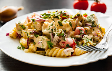 fusilli pasta salad with tomato, chicken breast, onion and olive with sauce in plate on dark wooden background - obrazy, fototapety, plakaty