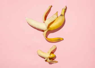 Sweet juicy opened little banana and opened big banana on pink table. Sexual life libido, penis size and potency concept. - obrazy, fototapety, plakaty
