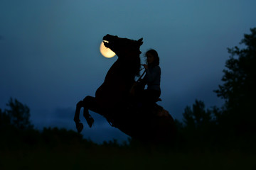Fantasy full moon with dark silhouette of the horse rider. Horseback  riding, woman under moonlight. Atmosphere moonlight horror background for halloweens nightmare. 