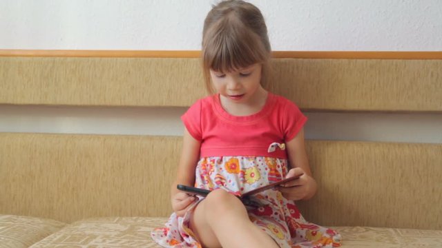 Little girl reading e-book on the sofa