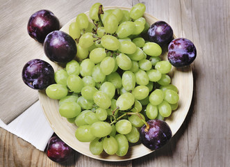 Fresh grapes and plums on a plate on a wooden background