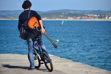 Santander, Spain. June 5, 2014. Young man with guitar on bicycle facing the sea