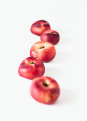 Selective focus composition of several fresh flat donut nectarines, red saturn nectarines or ripe fuzzless vineyard peaches on white background