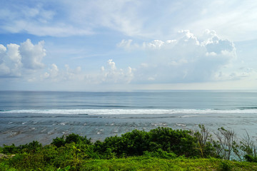 The coast of Uluwatu in Bali. Ocean and dense green grass. A huge cliff. Side view with copy space